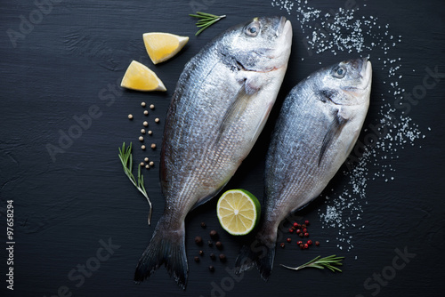 Top view of two uncooked dorada fishes on a black wooden surface
