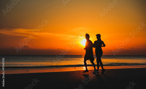 Young couple: man and woman run together on a sunset on lake coa