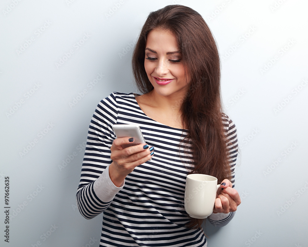 Happy casual woman texting sms and holding in hand cup of coffee Happy casual woman texting sms and holding in hand cup of coffee