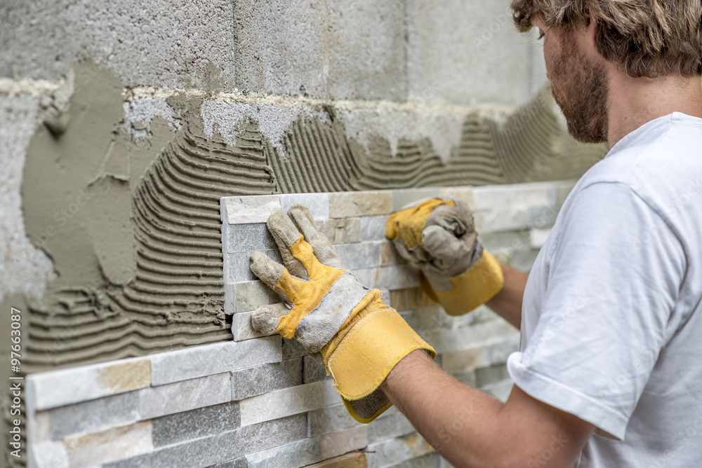 Man pressing an ornamental tile into a glue on a wall - obrazy, fototapety, plakaty 