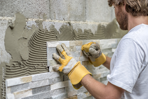 Man pressing an ornamental tile into a glue on a wall photo
