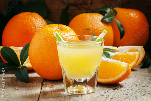 Orange juice in a glass with striped straws and large ripe orang