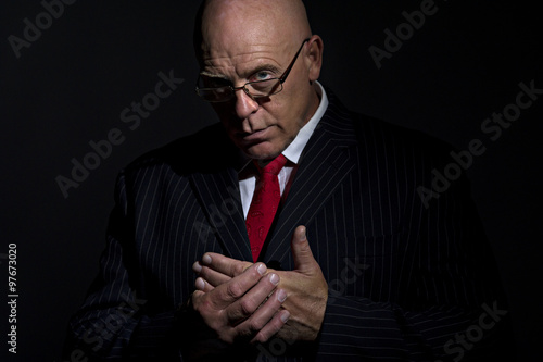 Portrait of mature male rubbing his hands together. He is looking into camera over the rim of his glasses