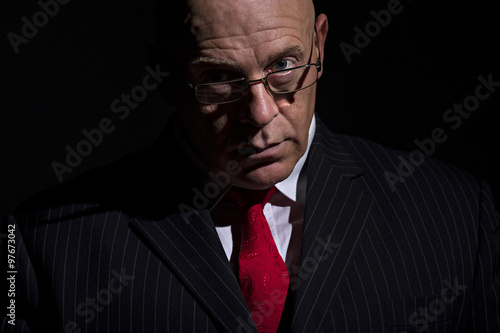 Portrait of mature male rubbing his hands together. He is looking into camera over the rim of his glasses
