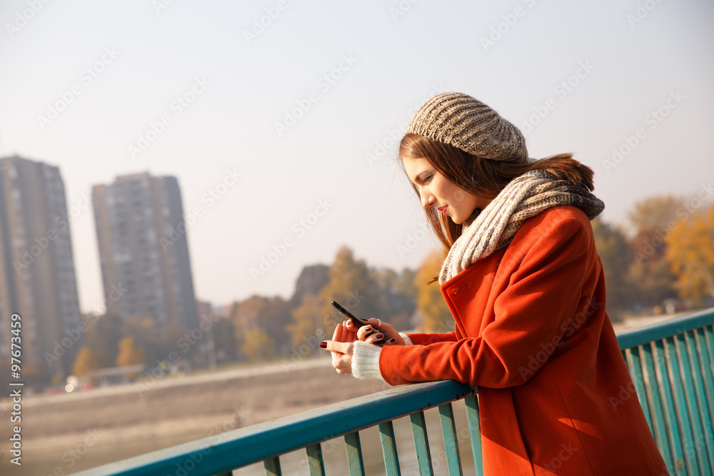 Portrait of a young woman on a bridge on a sunny autumn day, she in looking at phone. Natural light. Portrait of a young woman on a bridge on a sunny autumn day, she in looking at phone. Natural light.