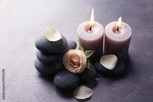 Relax concept - composition of aroma candles with pebbles and flower on grey background