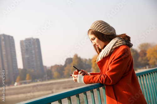 Portrait of a young woman on a bridge on a sunny autumn day, she in looking at phone. Natural light.