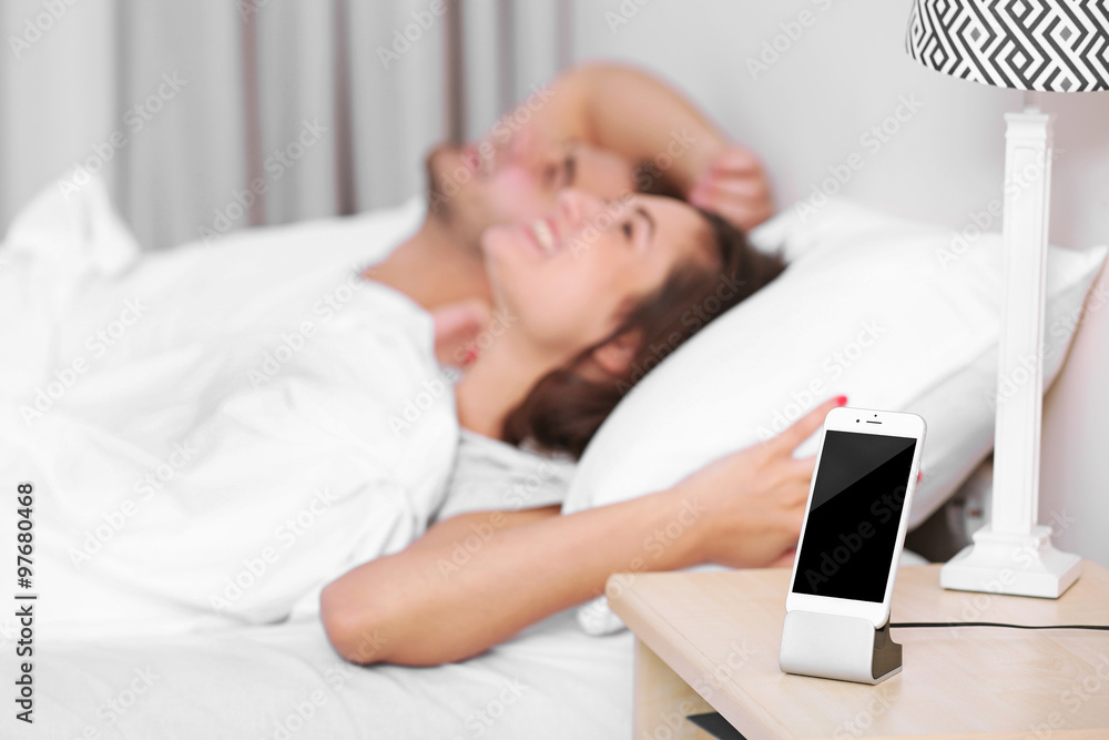 Happy couple waking up with mobile alarm clock Happy couple waking up with mobile alarm clock