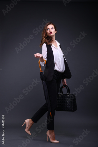 Business lady in a black jacket white shirt, umbrella, handbag on a dark background. Studio shot photo