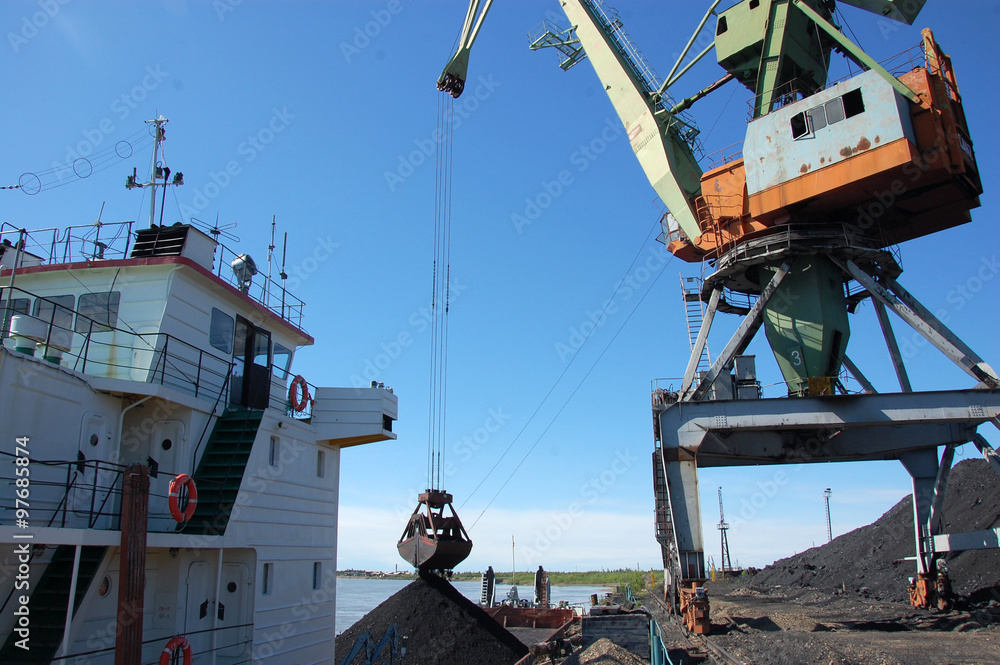 Fototapeta premium Dockside cargo crane loads coal at river port Kolyma