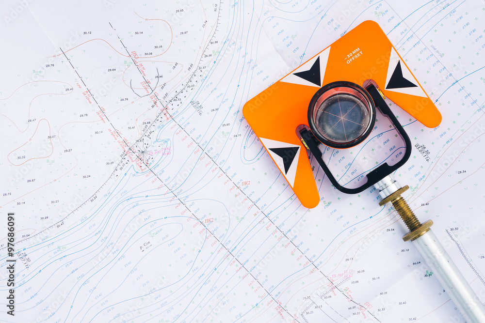 orange theodolite prism lies on a background geodetic maps of the area - obrazy, fototapety, plakaty 
