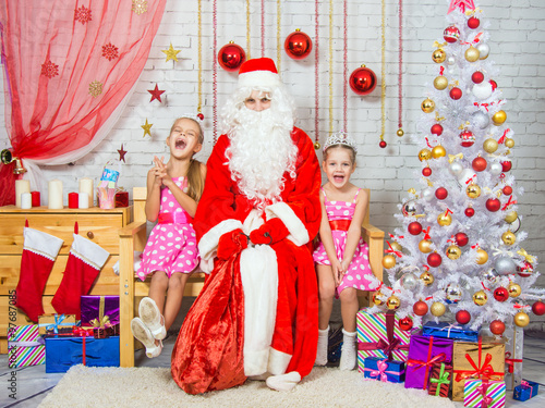 Happy girls and Santa Claus sitting on a bench in a Christmas setting
