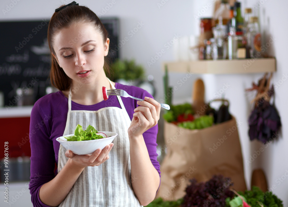 Young woman eating fresh salad in modern kitchen Young woman eating fresh salad in modern kitchen