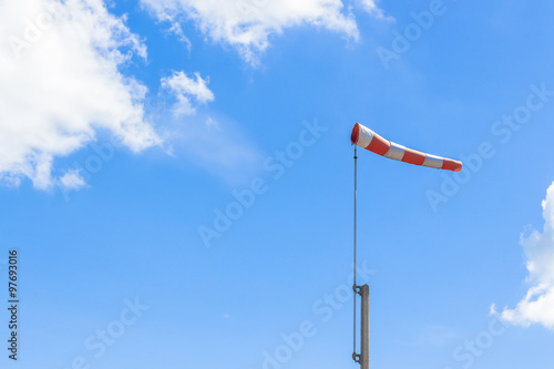 Red and white windsock blows against a blue sky