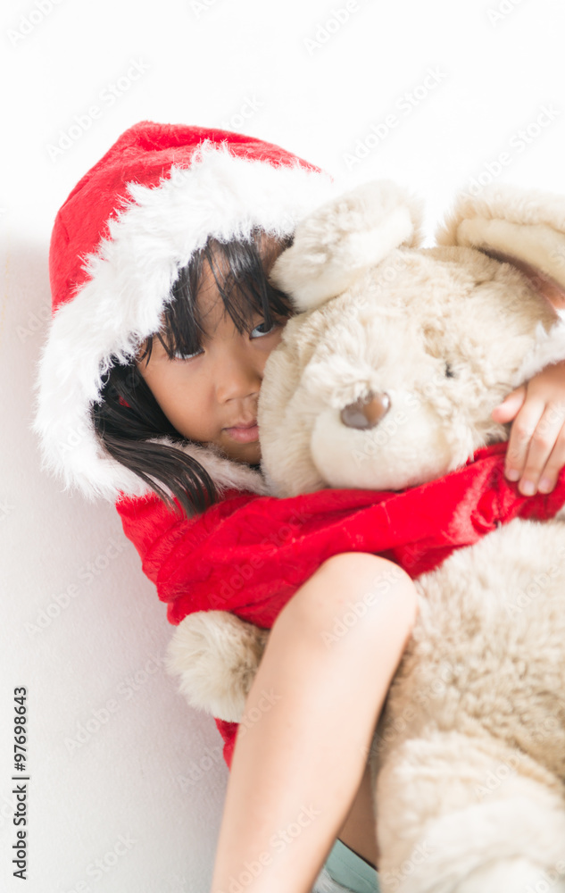 Little Asian girl in santa costume hugging bear doll on christma