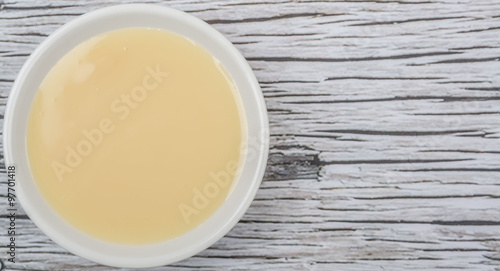 Sweet condensed milk in white bowl over wooden background photo