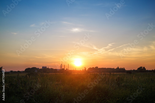 Sunset in the countryside. Bright sunshine and picturesque sky. Silhouettes of the village and the factory chimneys on the horizon.