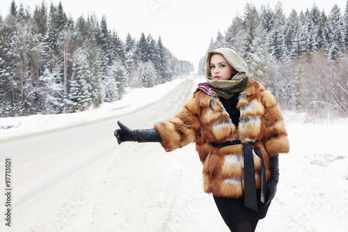 beautiful woman in fur coat waiting for the car on a winter road.girl in gloves