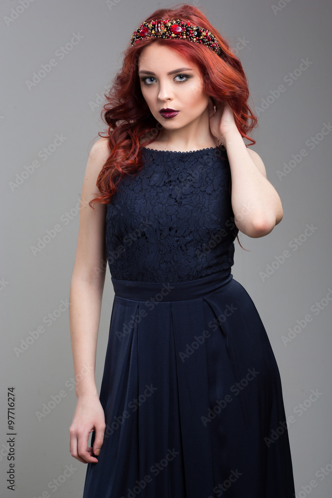 Beautiful red-haired fashion model posing in evening dress and in the diadem over dark background. female gestures of seduction. body language. touching her hair Beautiful red-haired fashion model posing in evening dress and in the diadem over dark background. female gestures of seduction. body language. touching her hair