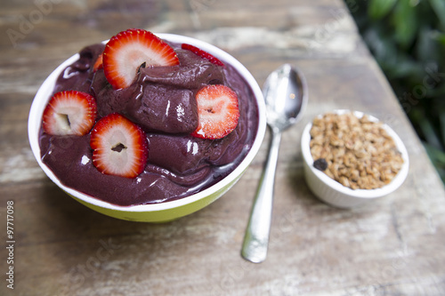 Bowl of fresh Brazilian acai garnished with strawberries and granola on a rustic wood table in Rio de Janeiro, Brazil