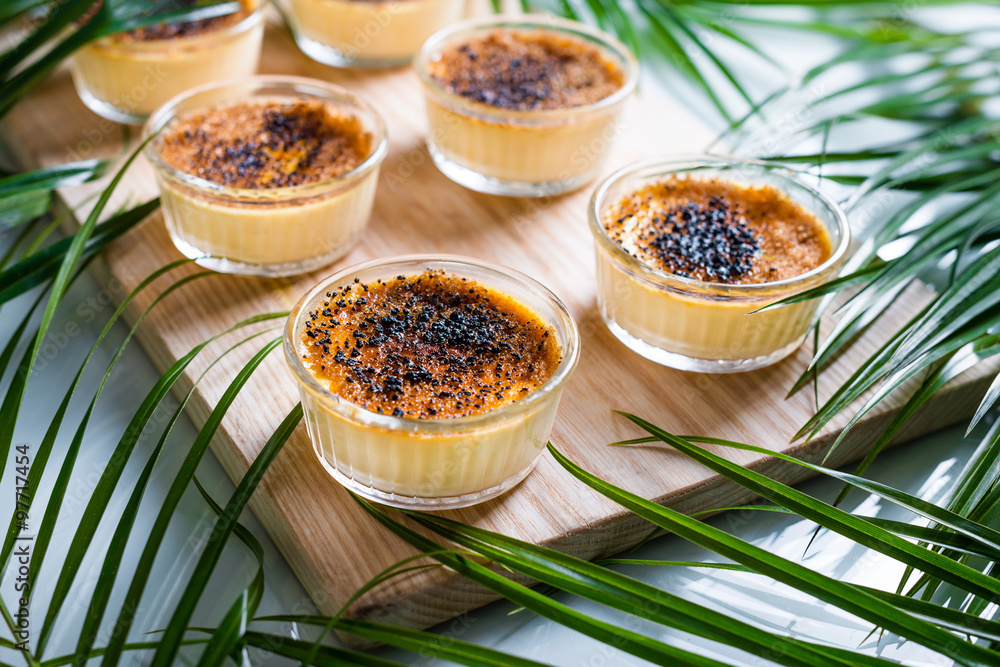 Creme brulee on wooden tray decorated with palm leaves. Traditional French vanilla cream dessert with caramelised sugar on top. Creme brulee on wooden tray decorated with palm leaves. Traditional French vanilla cream dessert with caramelised sugar on top.