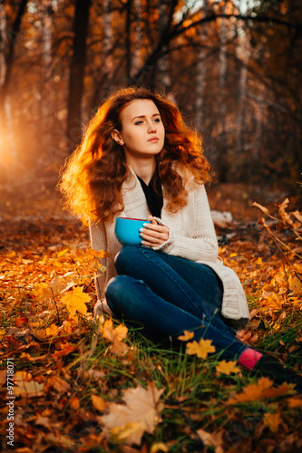 Young woman in a sweater and jeans relaxing drink tea on autumn background