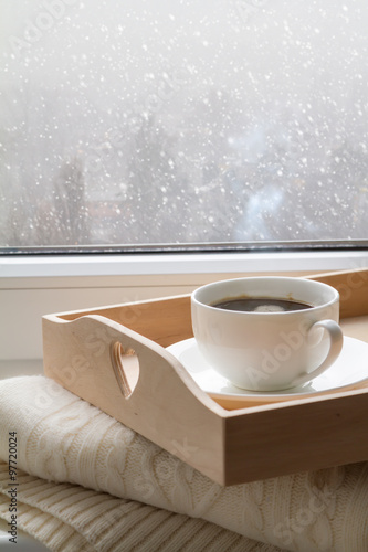 Coffee on tray and sweater in from of snowing winter