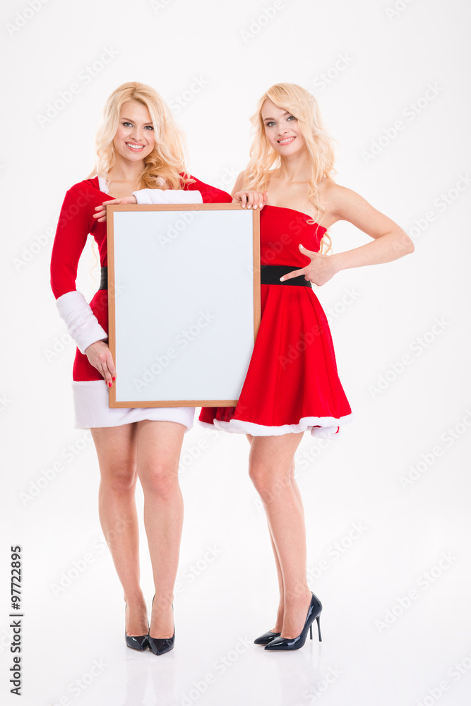 Sisters twins in red santa claus dresses with blank board Sisters twins in red santa claus dresses with blank board