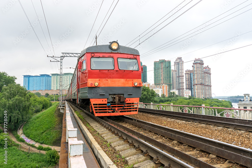 Red and grey suburban electric train moves towards on railroad turn vanishing against skyline background. Moscow, Russia. 
