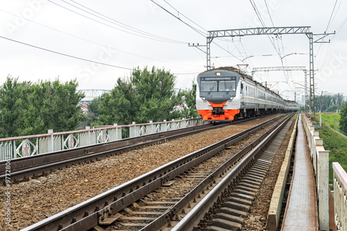 Red and grey suburban electric train moves towards on railroad turn vanishing against skyline background. Moscow, Russia. 