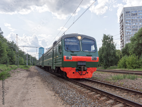 Green suburban electric train moves towards on railroad turn vanishing against skyline background. Moscow, Russia. 