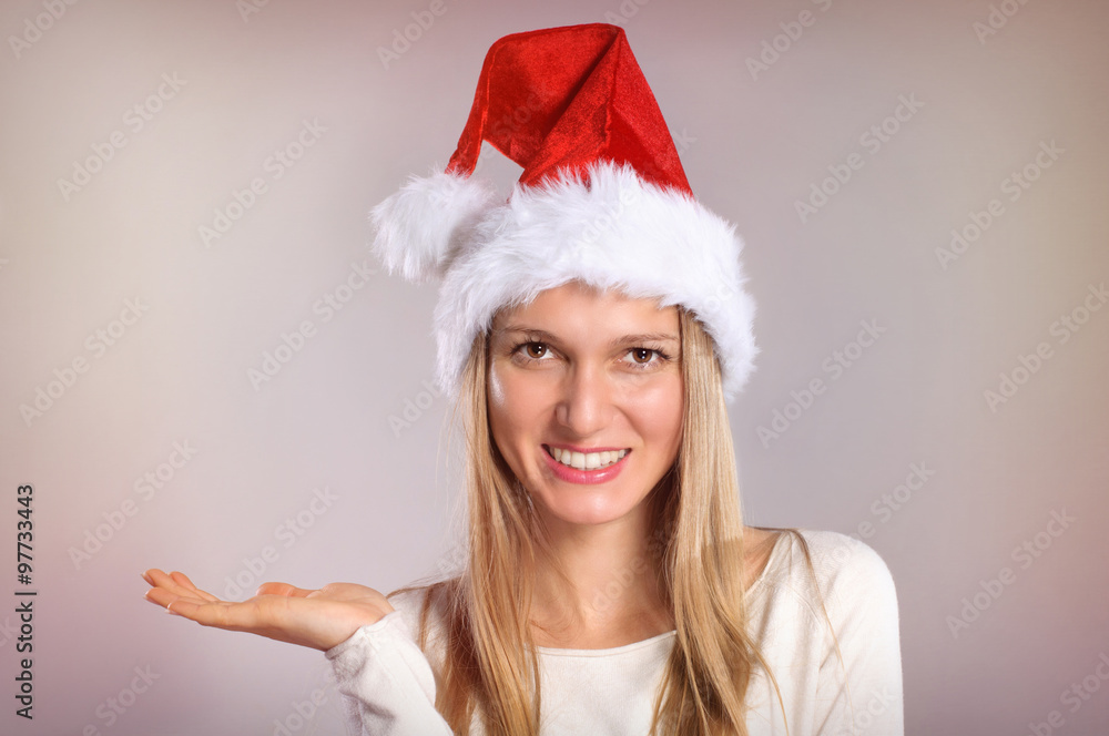 Beautiful woman with a Santa hat gestures palm up. Smiling Chris Beautiful woman with a Santa hat gestures palm up. Smiling Chris