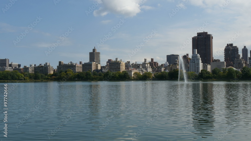 New York City Central Park fountain and urban Manhattan skyline with skyscrapers and trees with blue sky and white cloud 4K UHD New York City Central Park fountain and urban Manhattan skyline with skyscrapers and trees with blue sky and white cloud 4K UHD