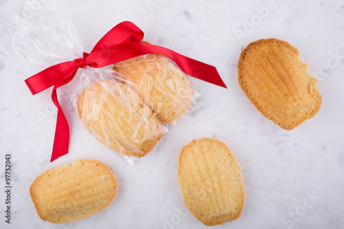 Madeleines wrapped with red ribbon on a white pastry board.