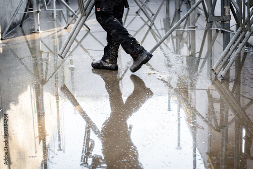 Construction site under water. Legs of a working man and his reflection in the water. Selective focus.