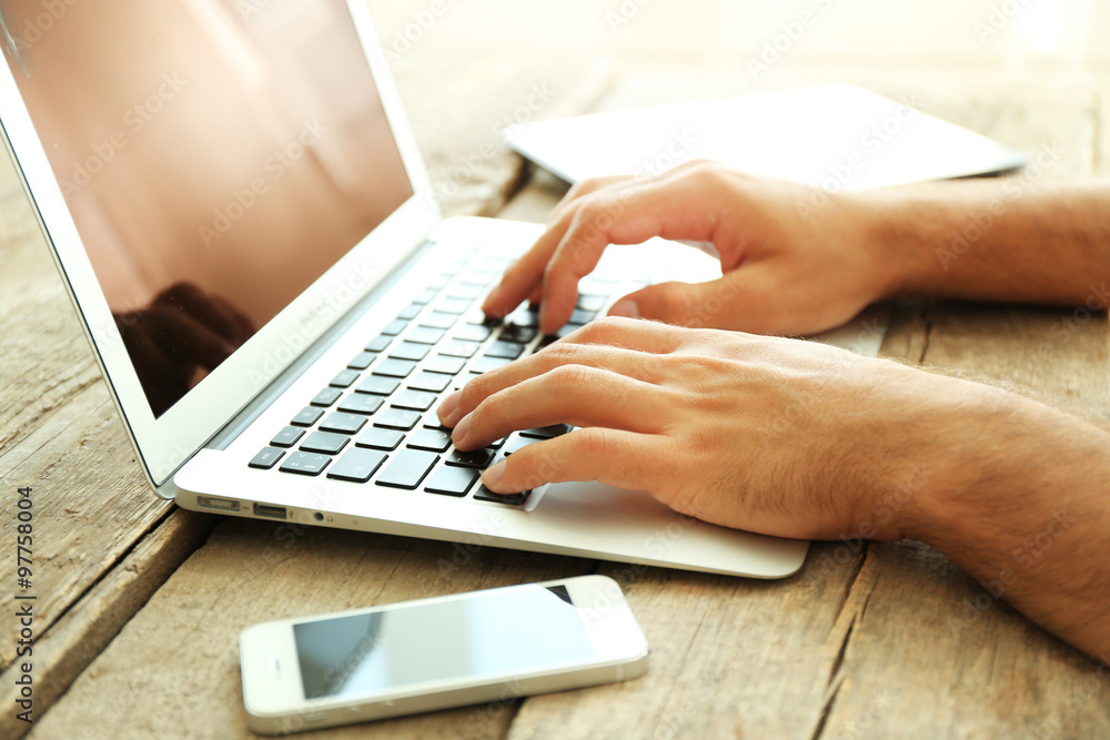 Male's hands taping on laptop on wooden table in office Male's hands taping on laptop on wooden table in office