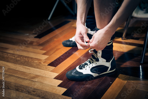 Closeup of young boxer's hands tying trainers on parquet background