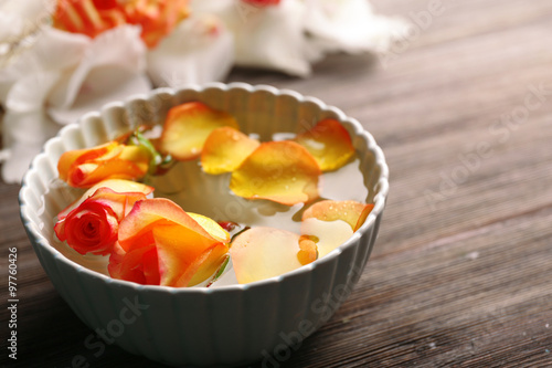 Beautiful orange rose and petals in a bowl of water on wooden background