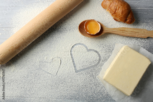 Heart of flour, croissant and wooden kitchen utensils on gray background