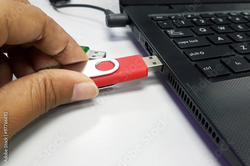 Close up of a woman hand plugging a pendrive on a laptop in soft focus photo