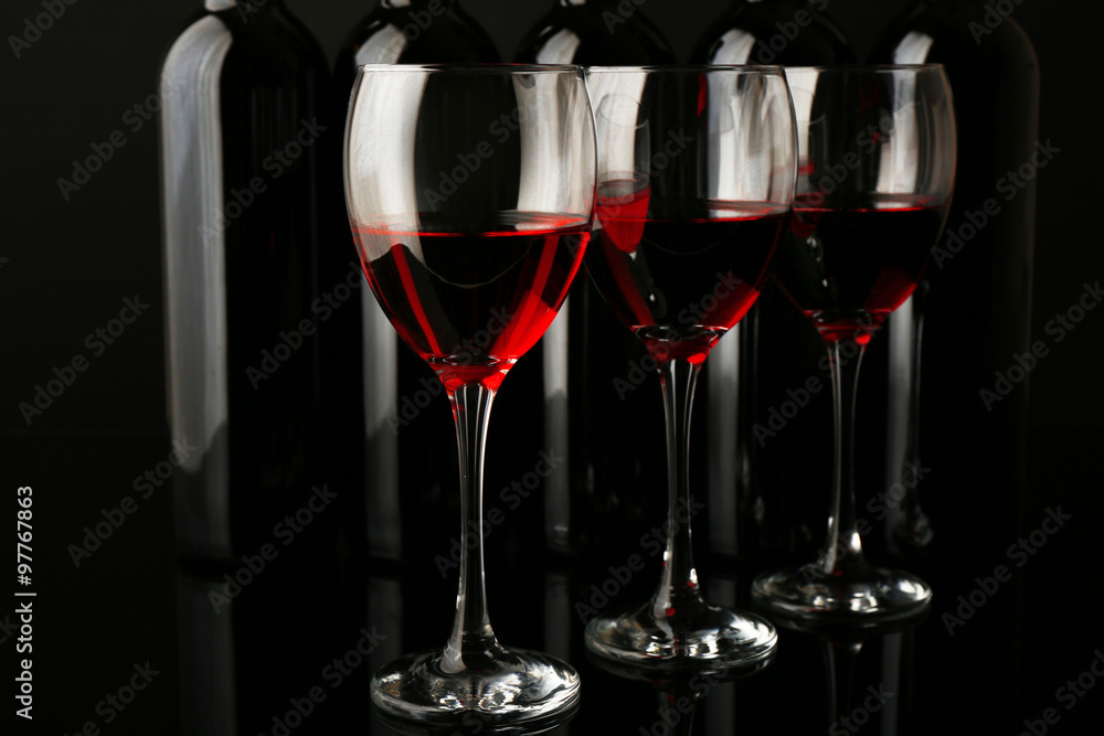 Wine glasses against bottles in a row on black background, close up Wine glasses against bottles in a row on black background, close up