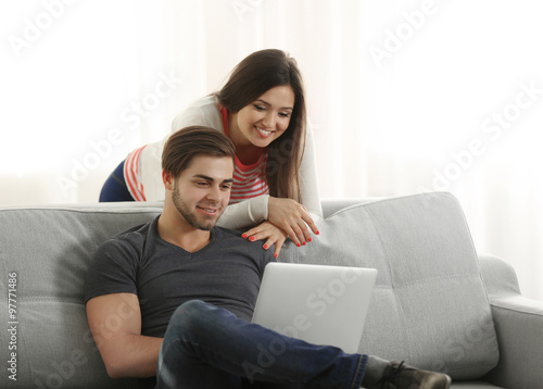 Young happy couple using laptop at home on light background