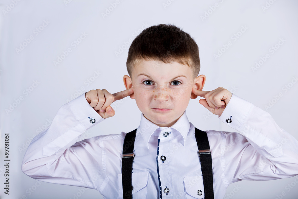 Angry, unhappy, irritated little boy covering ears, looking to camera over white background. Angry, unhappy, irritated little boy covering ears, looking to camera over white background.