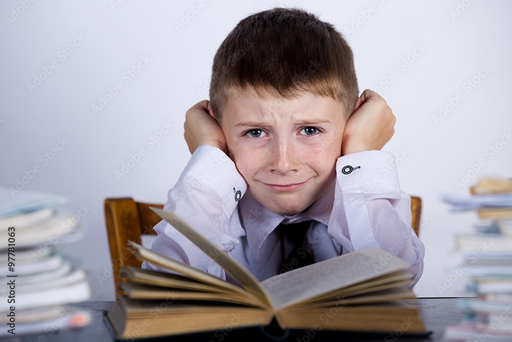 Little child stressed, tired, leaning on pile of books, isolated grey background.Upset bored child with a stack of books leaning on them.Education concept Little child stressed, tired, leaning on pile of books, isolated grey background.Upset bored child with a stack of books leaning on them.Education concept