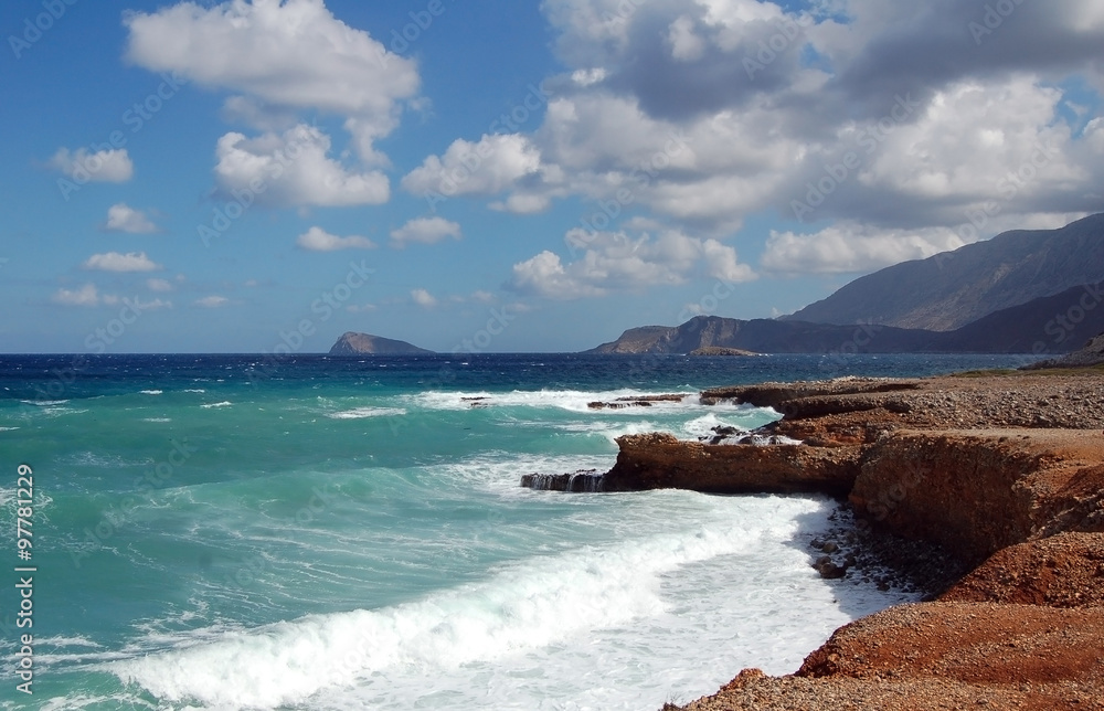 Waves on red rock sea shore with mountains and blue sky