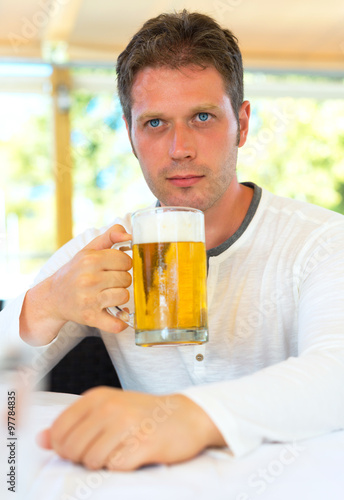 Handsome man with beer in summer cafe.