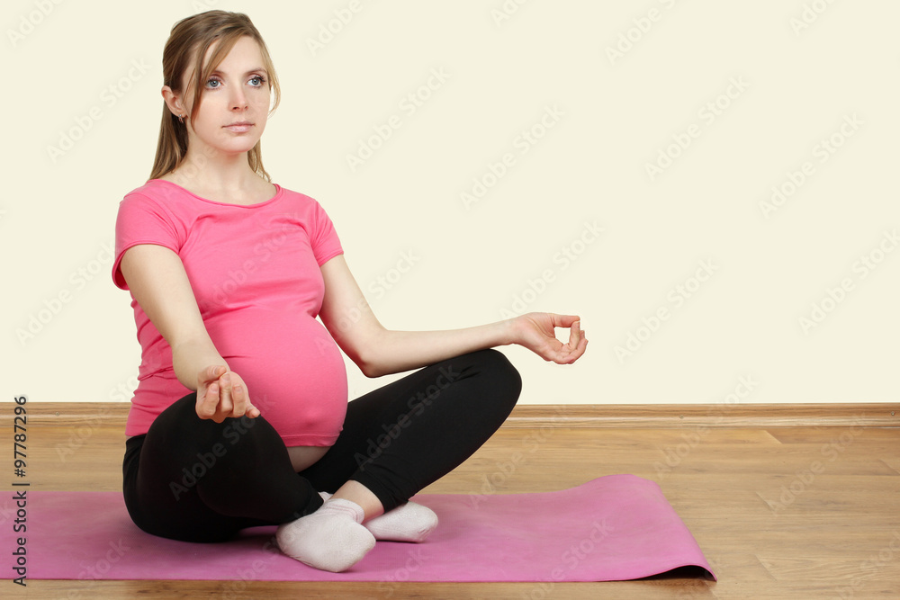 pregnant woman sitting on yoga Mat over white background