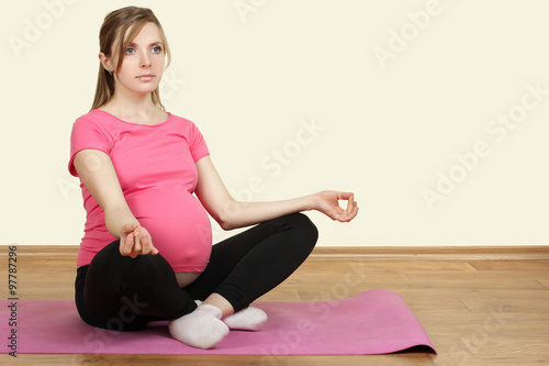 pregnant woman sitting on yoga Mat over white background