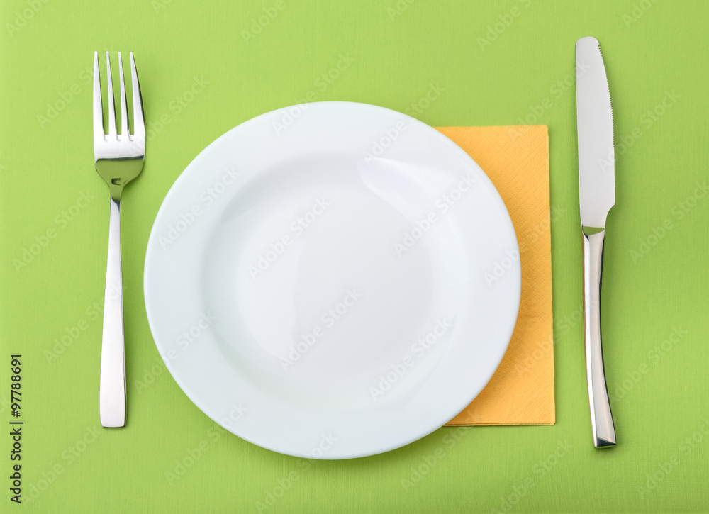 Empty plate, fork and knife on green background Empty plate, fork and knife on green background