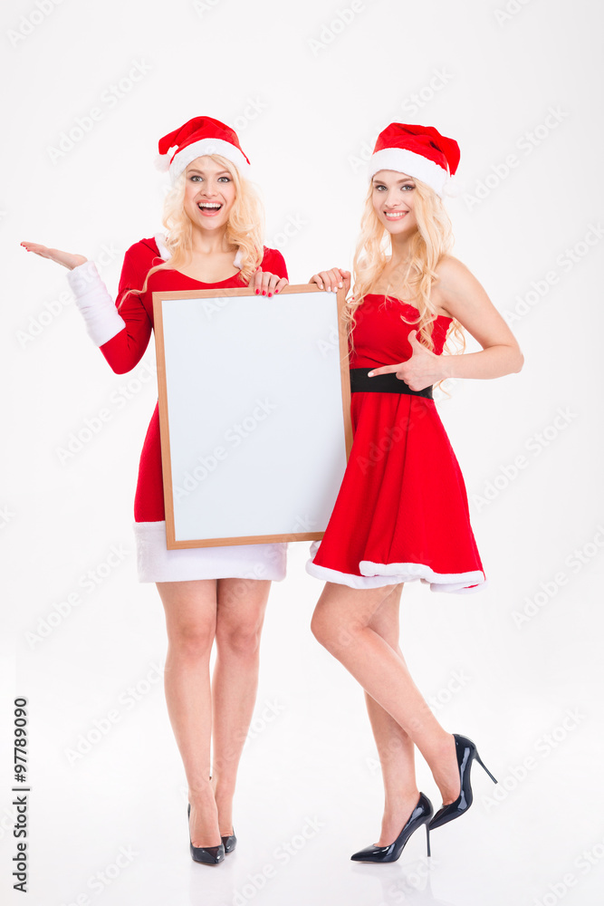 Two happy beautiful sisters twins pointing on blank board Two happy beautiful sisters twins pointing on blank board
